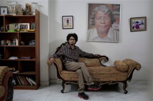 25-year-old Bangladeshi blogger Ananya Azad poses for a photograph at his house beside a portrait of his late father Humayun Azad, who was attacked a decade ago for his writings against Muslim extremism, in Dhaka, Bangladesh, Saturday, April 4, 2015. Ananya quit his job as a newspaper columnist and stopped writing blogs in recent months after receiving numerous threats for being critical of Islamic fundamentalism and politics driven by religion, but still posts critical comments on Facebook. Ananya says he's thinking about fleeing the country and spends much of his time indoors these days after a secularist blogger was hacked to death earlier this week in the streets of the capital, the second in less than a month. (AP Photo/ A.M. Ahad)