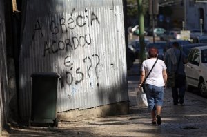People walk past a graffiti that reads in Portuguese: "Greece woke up, what about us?" in Lisbon, Thursday, May 21, 2015. European Central Bank head Mario Draghi said that "growth is too low everywhere" in Europe despite a modest recovery, during an ECB's conference on inflation and unemployment in Sintra, Portugal. (AP Photo/Francisco Seco)