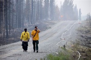 In this June 16, 2015 photo, two Nikiski Fire Department firefighters walk on a road near a fire-ravaged forest left behind by the Card Street fire in Sterling, Alaska. The wildfire moved rapidly northeast toward the Kenai National Wildlife Refuge and authorities have evacuated the Upper and Lower Skilak Lake campground. (Rashah McChesney/Peninsula Clarion via AP)