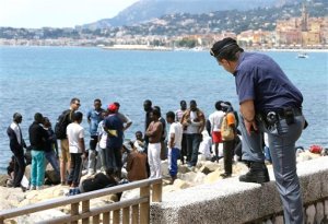 An Italian policeman looks at migrants gathered at the Franco-Italian border near Menton, southeastern France, Sunday, June 14, 2015. Some 150 migrants, principally from Eritrea and Sudan, attempted to cross the border from Italy and have been blocked by French and Italian gendarmes. (AP Photo/Lionel Cironneau)