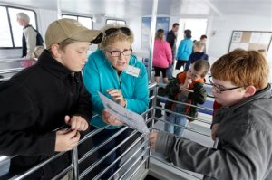 In a photo from Thursday, May 7, 2015,  in Alpena, Mich., volunteer Shari Davis points out details of a ship to students as they view a shipwreck in Thunder Bay. Thunder Bay National Marine Sanctuary is rolling out the buoys and starting another season of work on Lake Huron _ the highlight of which is searching for and studying shipwrecks. (AP Photo/Carlos Osorio)