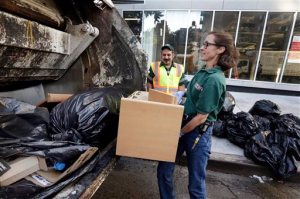 New York University professor and Department of Sanitation of New York anthropologist-in-residence Robin Nagle, right, puts some discarded refuse into the truck as she accompanies sanitation worker Joe Damiano, center,  during his morning rounds, Wednesday, Aug. 12, 2015, in New York. Nagle studies the refuse along the curbs of the nation's biggest city as a mirror into the lives of its 8.5 million residents. (AP Photo/Richard Drew)