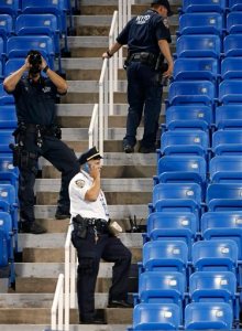 Police officers investigate the southwest corner of Louis Armstrong Stadium after a drone flew over the court, buzzing the players during a match between Flavia Pennetta, of Italy, and Monica Niculescu, of Romania, during the second round of the U.S. Open tennis tournament in New York, Thursday, Sept. 3, 2015. The drone crash-landed in the seats and can be seen to the right of the police officer on his phone. (AP Photo/Kathy Willens)