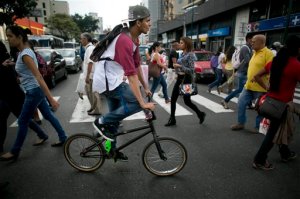 In this Sep. 4, 2015 photo, a cyclist rides his bike across a street in Caracas, Venezuela. Caracas Mayor Jorge Rodriguezs seemingly-futile bet on the bike has elicited so much praise. With street crime rampant, many residents feel safer riding in tinted-window SUVs with the doors locked than they do pedaling through lonely parks. So police have deployed 17 bike cops to patrol the red-asphalt paths. (AP Photo/Ariana Cubillos)