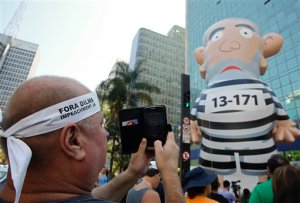 An anti-government demonstrators wearing a headband that reads in Portuguese "Dilma out, impeachment now,"  takes pictures of a giant inflatable in the likeness of Brazil's former President Luiz Inacio Lula da Silva in prison stripes, during a protest in Sao Paulo, Brazil, Sunday, Aug. 30, 2015. A convicted black market money dealer who turned state's evidence told lawmakers on Tuesday that Brazilian President Dilma Rousseff and her predecessor, former President Luiz Inacio Lula da Silva, knew of the sprawling corruption kickback scheme that has engulfed state-run oil company Petrobras. (AP Photo/Andre Penner)