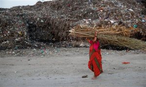 An Indian woman carries a bundle of dried branches and walks past a mound of garbage on the outskirts of Lucknow, India, Thursday, Sept. 24, 2015. India will confirm plans next week for a staggering 175 gigawatt growth in its renewable energy portfolio, Indian Environment Minister Prakash Javadekar said Thursday. India is one of the last major polluters yet to submit its plans for combating and coping with climate change to the United Nations, before the world's nations attempt to nail down a global climate pact in Paris in December. (AP Photo/Rajesh Kumar Singh)