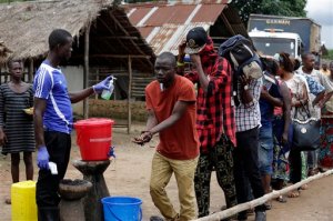 In this photo taken Wednesday, Aug. 12, 2015, a man takes checks people's temperature and helps to wash their hands as they leave Ebola quarantine, after Sierra Leone President Ernest Bai Koroma cut a tape to release the quarantine in the village of Massessehbeh on the outskirts of Freetown, Sierra Leone.  Five months after a man traveled to his home village for festivities marking the end of Ramadan, and died suddenly from Ebola, but now President Koroma came to cut down the fencing to mark the formal end of Sierra Leone's largest remaining Ebola quarantine. (AP Photo/Sunday Alamba)