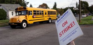 A school bus for a private school drives past a striking teacher in front of West Seattle Elementary School Wednesday, Sept. 9, 2015, in Seattle. Teachers in Seattle began walking picket lines after last-minute negotiations over wages and other issues failed to avert a strike in Washington state's largest school district. Classes for 53,000 Seattle Public Schools students were canceled Wednesday, on the scheduled first day of school. (AP Photo/Elaine Thompson)