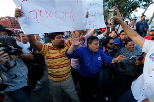 A protester holds up a sign in front of Jimmy Morales, the National Front of Convergence party presidential candidate, prior to a campaign rally in Guatemala City, Thursday, Oct. 22, 2015. The men equate Morales' party with the Guatemalan military, which has been accused of massive human rights abuses during the country's civil war. In Sunday's presidential runoff, Morales, who boasted of his outsider status on the campaign trail, faces Sandra Torres, a businesswoman and longtime political party operative who in a previous campaign divorced former President Alvaro Colom to try to get around a rule barring presidential relatives from seeking the office. (AP Photo/Moises Castillo)