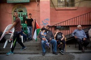 In this Monday, Oct. 12, 2015 photo, a Palestinian boy holds a national flag as he sits on his father's lap outside family home of Mohammed Ali, 19, in Shuafat refugee camp in Jerusalem. Ali was killed after he stabbed an Israeli policeman on Oct. 10 near Old City's Damascus Gate. (AP Photo/Dusan Vranic)