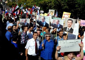 CORRECTS PUTIN's TITLE - This photo released by the Syrian official news agency SANA, shows Syrians holding photos of Syrian President Bashar Assad and Russian President Vladimir Putin, during a rally to thank Moscow for its intervention in Syria, in front of the Russian embassy in Damascus, Syria, Tuesday, Oct. 13, 2015. Insurgents fired two shells at the Russian embassy in the Syrian capital on Tuesday as hundreds of pro-government supporters gathered outside the compound to thank Moscow for its intervention in Syria. The placard at right with Arabic reads, "yes to Russian-Syrian cooperation." (SANA via AP)