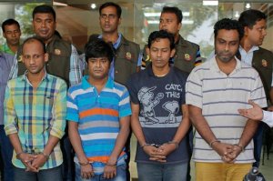 Bangladesh police personnel, standing behind, present before media four suspects they arrested in the killing of an Italian aid worker last month, in Dhaka, Bangladesh, Monday, Oct. 26, 2015. Italian aid worker Cesare Tavella was gunned down by motorcycle-riding assailants on Sept. 28 while jogging in the diplomatic quarter of Dhaka, Bangladesh's capital. Police said Monday that the alleged gunmen had confessed to being hired to attack "a white man" in order to destabilize the impoverished South Asian nation. (AP Photo/ A.M. Ahad)