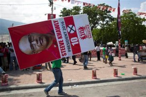 In this Oct. 10, 2015 photo, a man carries a campaign poster promoting presidential candidate Steeve Khawly, of the Bouclier political party, to a rally in Port-au-Prince, Haiti. For a few weeks at least, there's the promise of regular money to be made as human billboards, protesters for hire or paid shills for candidates amid a national election that features 54 presidential candidates, only a handful of whom have even faint name recognition among the vast majority of the population. (AP Photo/Dieu Nalio Chery)