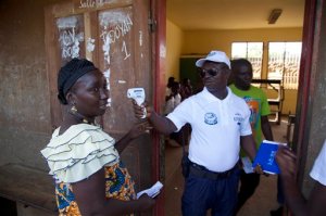 An electoral official takes a temperature reading to check a voter for Ebola before she casts her votes during presidential elections in Conakry, Guinea, Sunday Oct. 11, 2015. Guinea's president and main opposition candidate called for calm Sunday when they voted in the country's presidential election, after days of electoral clashes. (AP Photo/Youssouf Bah)