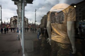 A mannequin seen through a glass window displays a T-shirt with a picture of a target hit by Russian air strike in Syria and words 'Support Assad', at the Russian Army Store in downtown Moscow, near the Kremlin, Russia, Thursday, Oct. 15, 2015, with the Historical museum is in the background. The Army Store has put on sale new products emblazoned with images of Russian air raids in Syria which began on Wednesday, Sept. 30, 2015. (AP Photo/Alexander Zemlianichenko)