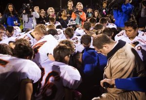 FILE - In this Friday, Oct. 16, 2015, file photo, Bremerton High assistant footbal coach Joe Kennedy, center in blue, kneels and prays after his team lost to Centralia in Bremerton, Wash. The coach of a Washington state high school football team who prayed at games despite orders from the school district to stop has been placed on paid administrative. Bremerton School District officials said in a statement late Wednesday, Oct. 28, 2015, that assistant football coach Joe Kennedy's leave was necessitated because of his refusal to comply with district directives that he refrain from engaging in overt, public religious displays on the football field while on duty as a coach.   ( Lindsey Wasson/The Seattle Times via AP) OUTS: SEATTLE OUT, USA TODAY OUT, MAGAZINES OUT, TELEVISION OUT, SALES OUT. MANDATORY CREDIT TO: LINDSEY WASSON / THE SEATTLE TIMES.