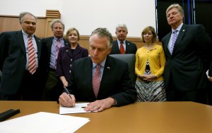 Virginia Governor Terry McAuliffe, center, signs an executive action to prevent gun violence as from left to right, U.S. Sen. Tim Kaine, D-VA, Andy Parker, his wife Barbara Parker, parents of slain WDBJ-TV reporter Alison Parker, Virginia Attorney General Mark Herring, Lori Haas, whose daughter Emily was injured in the VA Tech shootings, and Virginia Secretary of Public Safety and Homeland Security Brian Moran watch during a press conference in Richmond, Va Thursday, Oct. 15, 2015. (Bob Brown /Richmond Times-Dispatch via AP) MANDATORY CREDIT (