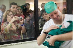 FILE - In this Aug. 2, 2012 file photo, relatives watch as Romulo Coelho holds his newborn daughter, Hadassa, birthed via cesarean section at the Perinatal Clinic in Rio de Janeiro. In clinics like Perinatal, most new parents have medical insurance that cover the $4,200 price tag of the C-sections, plus a three-day stay in a private room. But that cost can rise considerably. (AP Photo/Felipe Dana, File)