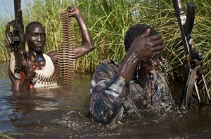 FILE - In this Saturday, Sept. 20, 2014 file photo, rebel soldiers patrol and protect civilians from the Nuer ethnic group as the civilians walk through flooded areas to reach a makeshift camp for the displaced situated in the United Nations Mission in South Sudan (UNMISS) base in the town of Bentiu, South Sudan. A long-awaited report by African Union investigators, released lated Tuesday, Oct. 27th, 2015 says mass graves have been discovered in South Sudan, cites horrific crimes against civilians including forced cannibalism, and disputes that there was a coup attempt by former Vice President Riek Machar in December 2013, finding that the conflict began with a skirmish between members of the presidential guard in the capital Juba. (AP Photo/Matthew Abbott, File)