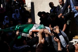 A Palestinian boy looks as mourners carry the body of  27-year-old Abdallah Shalaldeh, during his funeral in the West Bank village of Sa'ir, near Hebron, Thursday, Nov. 12, 2015. Israeli forces disguised in traditional Arab outfits, including one impersonating a pregnant woman and others appearing to have fake facial hair, burst into a hospital overnight Thursday, killing Shalaldeh during an arrest raid caught on video. (AP Photo/ Nasser Shiyoukhi)
