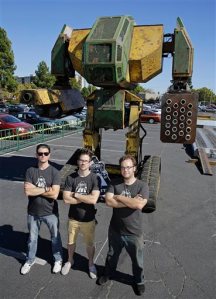 In this photo taken Friday, Oct. 9, 2015, MegaBots founders from left, Brinkley Warren, Matt Oehrlein and Gui Cavalcanti stand below their 15-foot tall, piloted Mk.II robot at the Pioneer Summit in Redwood City, Calif. Let the giant robot wars begin. A team of American engineers challenged a group in Japan to a battle for robot supremacy, and the Japanese said bring it on. So Oakland-based MegaBots has launched a Kickstarter campaign to raise money to turn the Mk.II, into a real fighting machine, ready for hand-to-hand combat. (AP Photo/Eric Risberg)