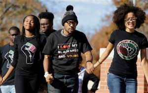 Jonathan Butler, center, is helped onto a stage before addressing a crowd following the announcement that University of Missouri System President Tim Wolfe would resign Monday, Nov. 9, 2015, at the university in Columbia, Mo. Butler has ended his hunger strike as a result of the resignation. (AP Photo/Jeff Roberson)