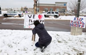 Bethany Winder, a nurse who lives in Colorado Springs, Colo., plants a sign in support of Planned Parenthood just south of its clinic as police investigators gather evidence near the scene of Friday's shooting at the clinic Sunday, Nov. 29, 2015, in northwest Colorado Springs. (AP Photo/David Zalubowski)