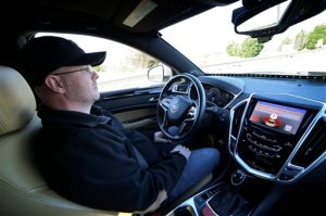 This Friday, Nov. 13, 2015, photo provided by Virginia Tech shows Greg Brown, technology development program administration specialist, sitting behind the wheel of a self-driving car during a test ride on a local street in Blacksburg, Va. The vehicle's alert system is handing over control to Brown as it disengages from self-driving mode. (Justin Fine/Virginia Tech via AP)