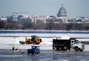 Workers remove snow on the tarmac at Ronald Reagan National Airport, with the U.S. Capitol dome seen behind, Sunday, Jan. 24, 2016 in Arlington, Va. Millions of Americans began digging out Sunday from a mammoth blizzard that set a new single-day snowfall record in Washington and New York City. (AP Photo/Alex Brandon)