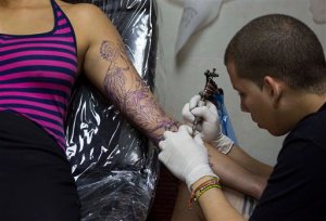 In this Feb. 5, 2016 photo, tattoo artist Mauro Coca works on a tropical bird down the length of arm of Julivic Marquez's arm in Havana, Cuba. The studio where Coca works, La Marca, or The Brand, is an example of Cuba's new acceptance of tattooing. The shop opened a year ago on one of Old Havana's busiest streets and has inked hundreds of tattoos for a mix of Cuban and foreign clients. It's been used as a space for government-sponsored art events and its managers say they've never had any trouble with the state despite their lack of a license explicitly permitting tattooing. (AP Photo/Desmond Boylan)