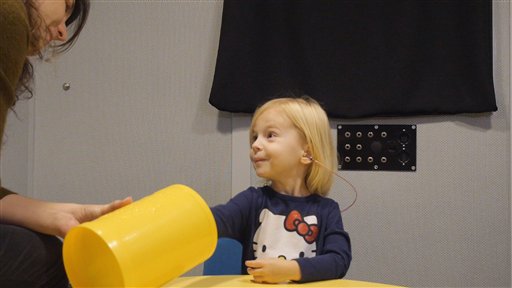In this images from video provided by University of North Carolina at Chapel Hill, a toddler participates in a speech perception experiment in a laboratory at the University of North Carolina in Chapel Hill, N.C.. The toddler was conditioned to put a block in the bucket whenever she heard the target word. From the cacophony of day care to the buzz of TV and electronic toys, noise is more distracting to a child's brain than an adult's, and new research shows it can hinder how youngsters learn. In fact, one of the worst offenders when a tot's trying to listen is other voices babbling in the background, researchers said Saturday at a meeting of the American Association for the Advancement of Science. (Emily Buss/University of North Carolina at Chapel Hill via AP)