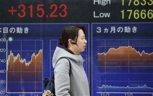 A woman walks by an electronic stock board of a securities firm in Tokyo, Monday, Feb. 1, 2016. Chinese stocks fell Monday after a weak manufacturing report while Japan extended gains following its central bank's introduction of a negative interest rate policy to boost lending by banks. Other markets were mixed. (AP Photo/Koji Sasahara)