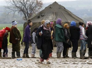 A refugee woman walks through the mud, carrying tea and bread as others are waiting in line, in a makeshift camp at the northern Greek border post of Idomeni, Wednesday, March 16, 2016. Hundreds of migrants and refugees walked out Monday of an overcrowded camp on the Greek-Macedonian border, determined to use a dangerous crossing to head north but were returned to Greece. (AP Photo/Boris Grdanoski)