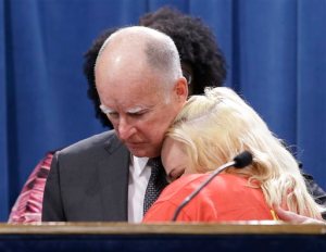 FILE - In this Monday, March 28, 2016 photo, Gov. Jerry Brown is hugged by Holly Dias, a Burger King employee who praised Brown's announcement of proposed legislation to increase the state's minimum wage to $15 per hour by 2022, during a news conference in Sacramento, Calif. On Monday, April 4, 2016, Brown is set to sign the legislation into law in Los Angeles. (AP Photo/Rich Pedroncelli)