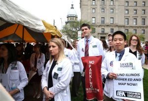 Medical students from Southern Illinois University School of Medicine listen to speakers during a rally supporting increased funding to education held near the state Capitol complex in Springfield on Wednesday, April 20, 2016. The rally, themed Save Higher Education: No Future Without Funding, was sponsored by the Illinois Coalition to Invest in Higher Education, and was attended by hundreds of other college students from throughout the state. (David Spencer/The State Journal-Register via AP) NO SALES, MANDATORY CREDIT