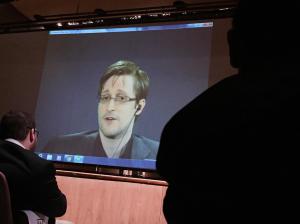 FILE- In this Feb. 17, 2016, file photo, former National Security Agency contractor Edward Snowden, center, speaks via video conference to people in the Johns Hopkins University auditorium in Baltimore. The Intercept, an online news site whose founding editors were the first to publish documents leaked by Snowden, released on Monday, May 16, the first batch of nine years' worth of the newsletters, which offer a behind-the-scenes glimpse into the NSAs work. (AP Photo/Juliet Linderman, File)