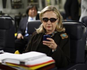 FILE - In this Oct. 18, 2011, file photo, then-Secretary of State Hillary Rodham Clinton checks her Blackberry from a desk inside a C-17 military plane upon her departure from Malta, in the Mediterranean Sea, bound for Tripoli, Libya. The presidential campaigns of Clinton and Donald Trump are both trying to prevent the public release of videos that are critical to legal cases involving the candidates.(AP Photo/Kevin Lamarque, Pool, File)