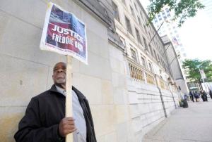 FILE- In this June 9, 2016 file photo, Arthur B. Johnson Jr., of Baltimore, demonstrates alone outside Baltimore's Courthouse East on the first day of the trial of Officer Caesar Goodson, one of six Baltimore city police officers charged in connection to the death of Freddie Gray, in Baltimore. More than a year after Freddie Gray's death, the same streets that exploded in fury and flame are calm. Despite back-to-back acquittals for officers charged in Gray's death, the physical protest movement that helped topple the careers of both the police commissioner and the mayor has dissipated, leaving activists exploring other avenues for change. (AP Photo/Steve Ruark, File)