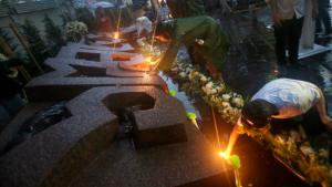 Thai activists lean over the Oct. 6 Memorial to offer lighted candles at Thammasat University in Bangkok, Thailand, Thursday, Oct. 6, 2016. Buddhist monks, mourners, activists and others gathered Thursday to mark the 40th anniversary of one of the darkest days in Thailand's history, when police killed scores of university students at a peaceful protest, and ghoulish vigilantes defiled the dead. (AP Photo/Sakchai Lalit)