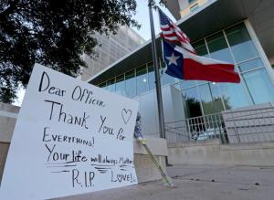 An American flag and a Texas state flag fly at half-staff at San Antonio Police Department headquarters near a sign and flowers left by Lucy Aldaba after Det. Benjamin Marconi was fatally shot Sunday, Nov. 20, 2016, in San Antonio. Marconi was writing out a traffic ticket to a motorist when he was shot to death in his squad car Sunday outside police headquarters by another driver who pulled up from behind, authorities said. (Edward A. Ornelas/The San Antonio Express-News via AP)