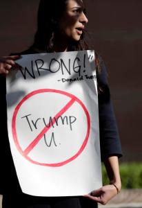 Senya Merchant holds a sign against President-elect Donald Trump's now-defunct Trump University Friday, Nov. 18, 2016, in San Diego. Trump agreed Friday to pay $25 million to settle several lawsuits alleging that his former school for real estate investors defrauded students who paid up to $35,000 to enroll in Trump University programs.(AP Photo/Gregory Bull)